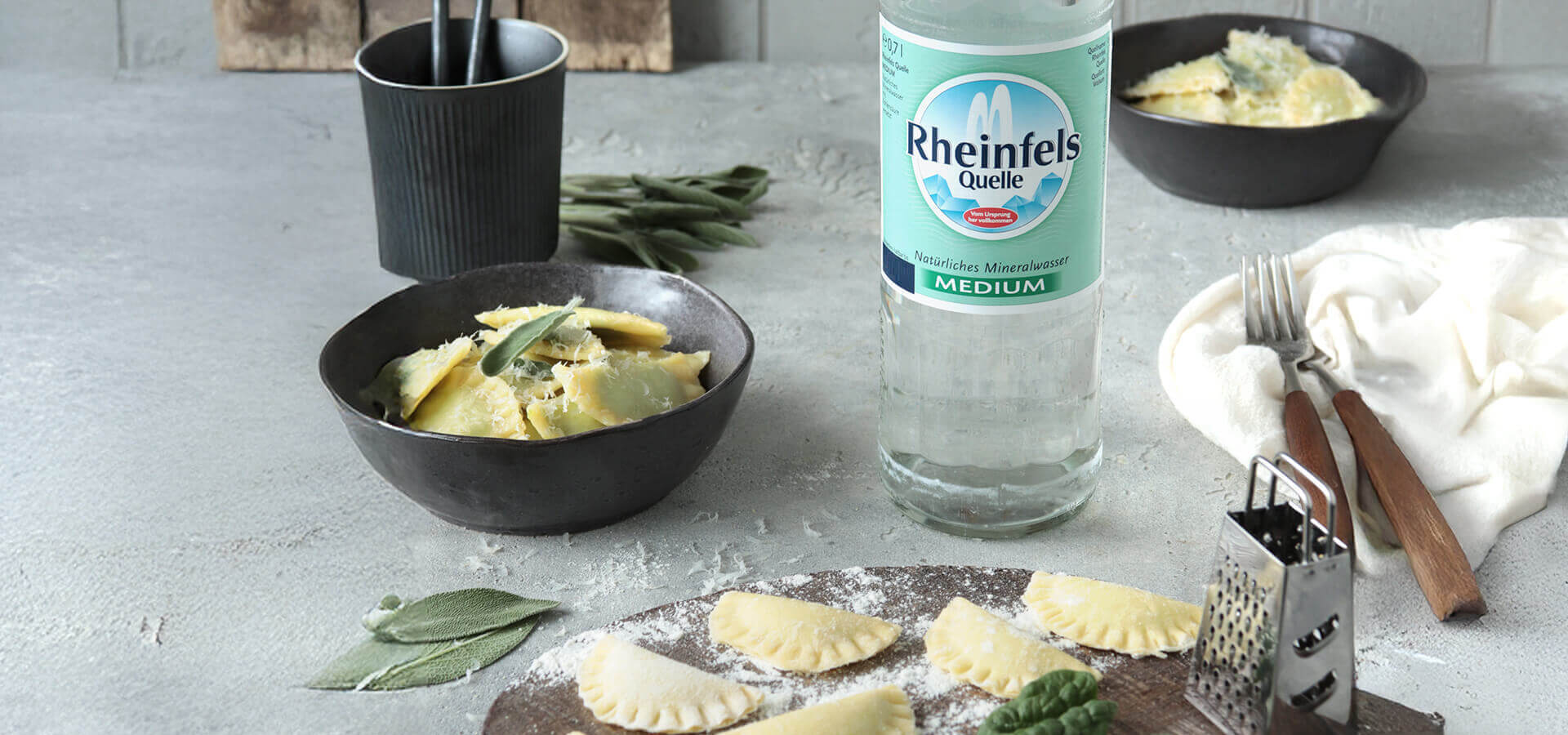 Selbstgemachte Pasta auf einem Holzbrett neben einer Flasche Rheinfels Quelle Medium