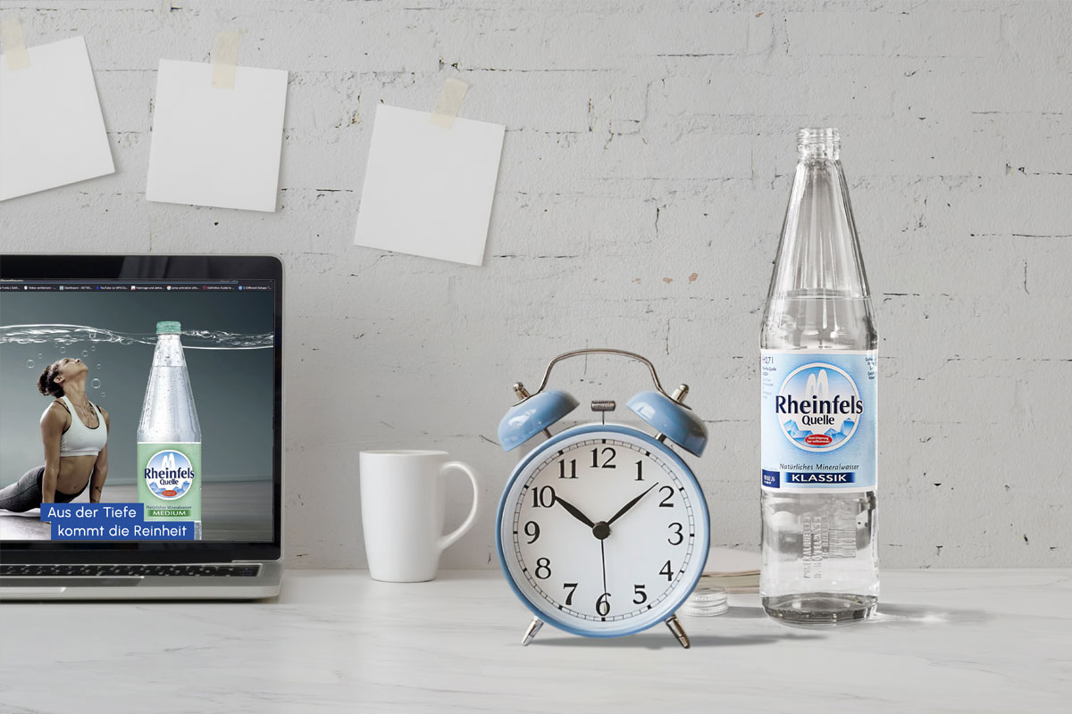 Rheinfels Quelle Klassik Flasche steht auf Tisch mit Wecker, aufgeklappten Laptop und Kaffeetasse
