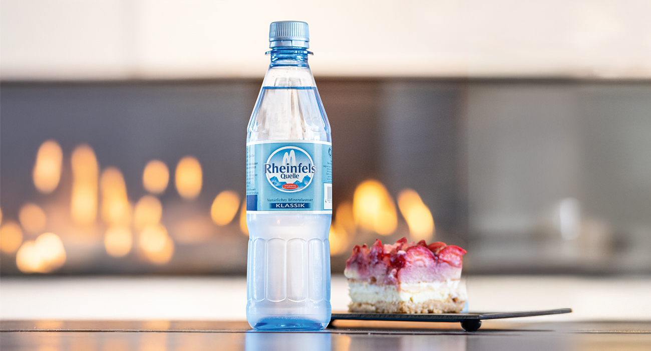 Rheinfels Quelle Klassik in 0,5 Liter PET Mehrweg steht auf einer Theke neben einem Stück Kuchen.